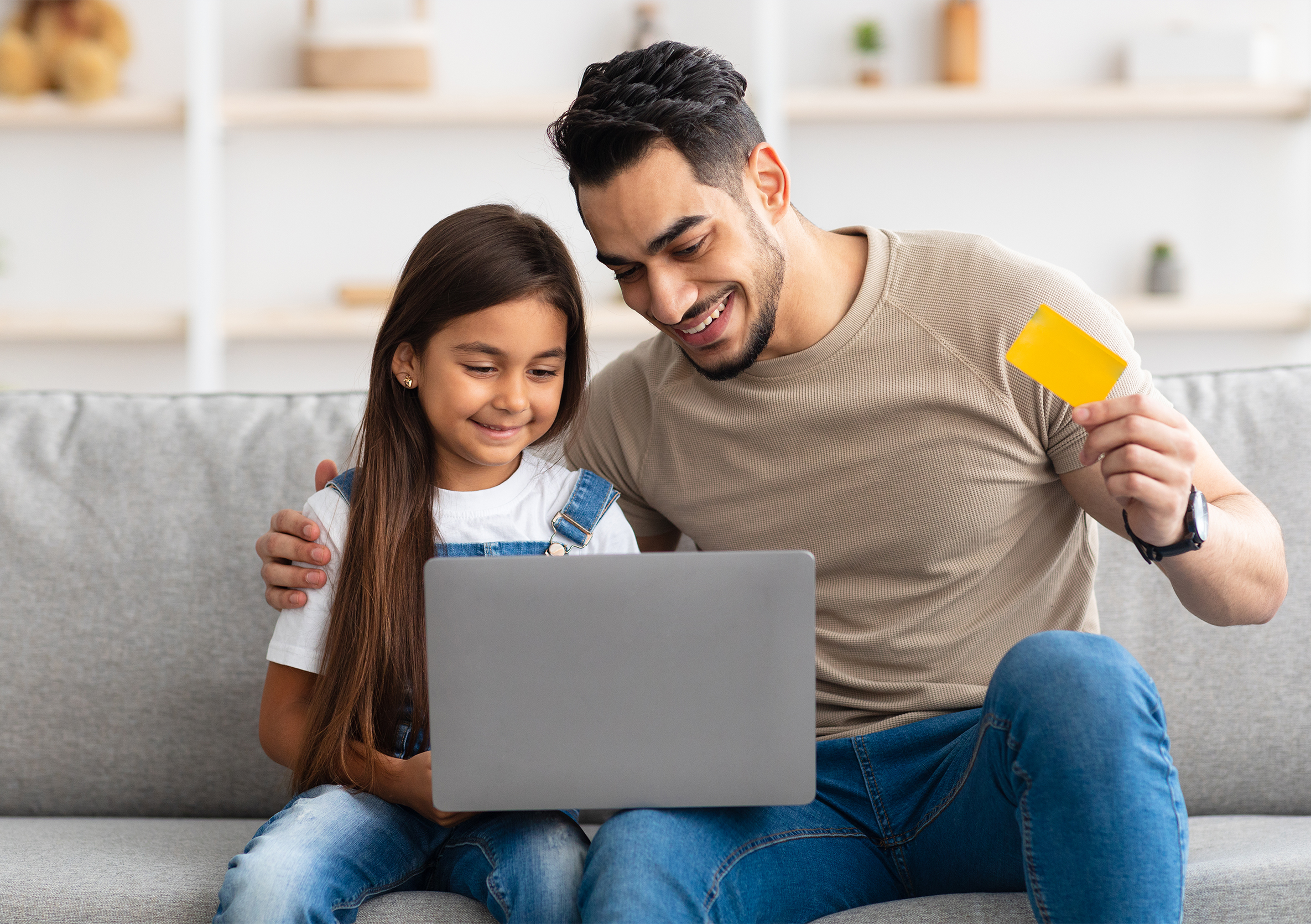 Father and daughter holding a gift card and sitting in front of a computer screen.